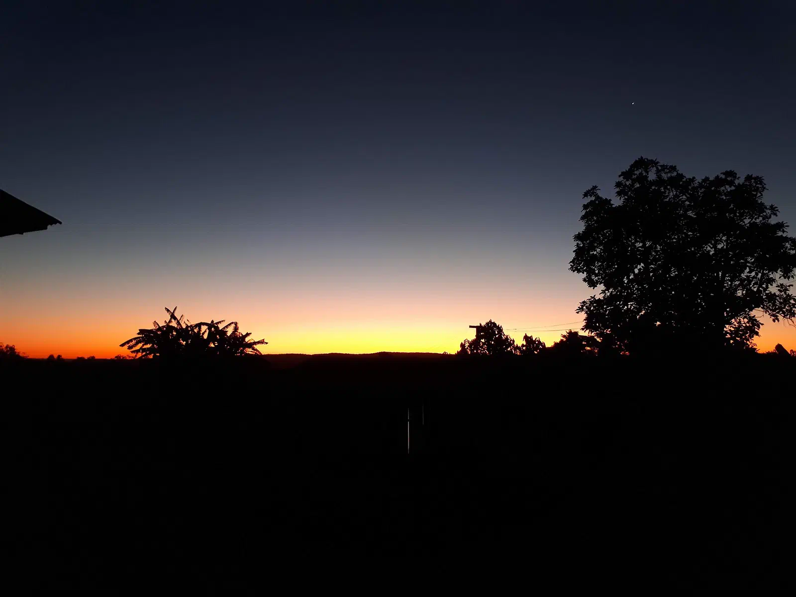 Crepúsculo alaranjado no horizonte, com silhuetas de árvores no extremo-oeste catarinense